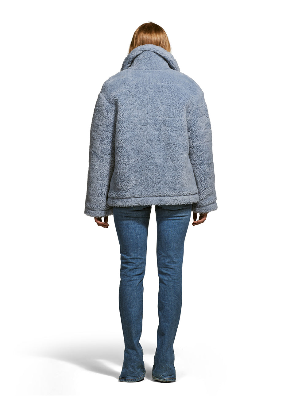 Model wearing the Robin, a hip-length teddy-inspired faux-fur sherpa shell in sky color from the rear.