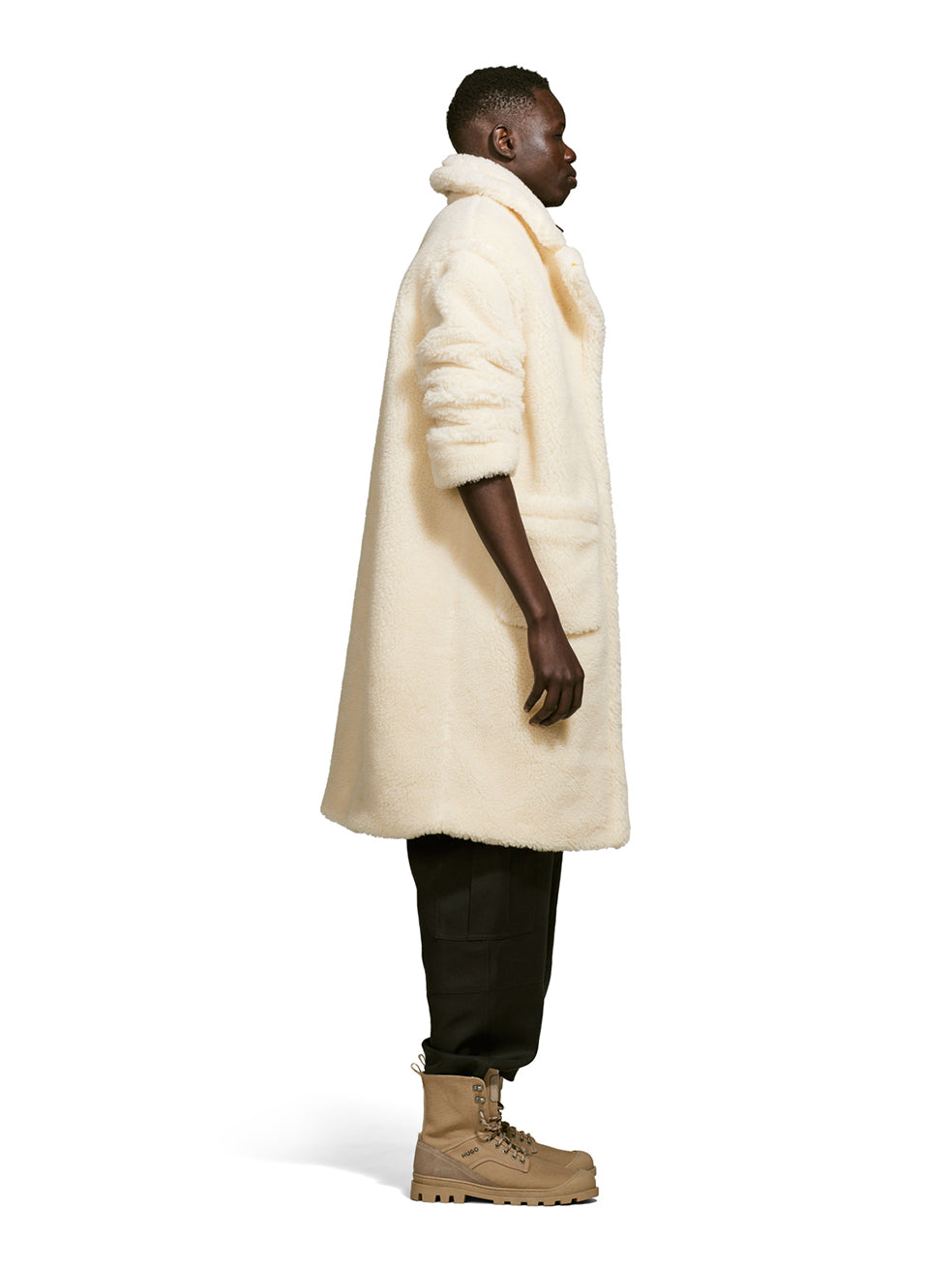 Male model wearing a teddy-inspired faux-fur sherpa shell in cream color on a white background from the side.
